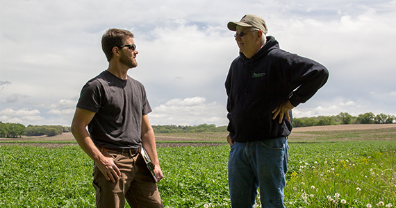 Staff member talking with a farmer surrounded by a green crop field