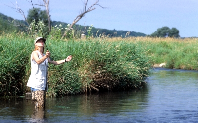 person fishing in waders while stand in a creek holding a fly fishing pole