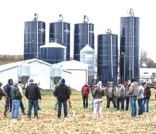 group of people talking in a field in front of farm with silos in background