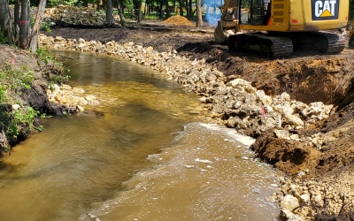 stream with rock placed at edge to prevent erosion, back hoe in background
